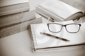 A workplace, where old books, notepad, pencil and glasses lie