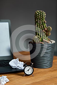 Workplace, wooden office desk with clock, sheet of paper, laptop, notebook, crumpled paper
