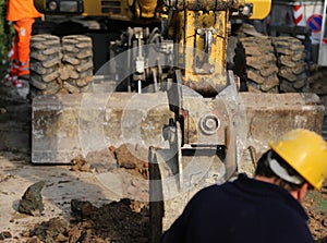 Works on a road construction site with the digger and the worker