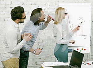 Workshop of businesswoman in office. Blonde woman draws graphs and diagrams on a white board. Male colleagues came