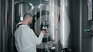 workshop of contemporary craft brewery, man is viewing dark beer in glass, standing between tanks