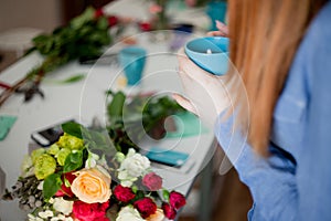 Workshop florist, making bouquets and flower arrangements. Woman resting with Cup of tea in hands. Soft focus