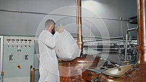 workshop of modern brewery, technologist is pouring malt into copper tank, brewing beer