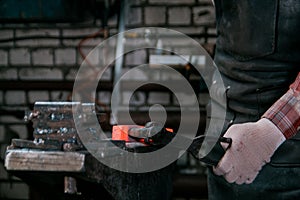 Workspace of blacksmith. Blacksmith working in gloves with red hot metal at anvil in a forge