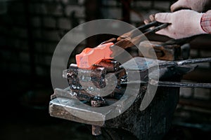 Workspace of blacksmith. Blacksmith working in gloves with red hot metal workpiece of new hammer at anvil in a forge