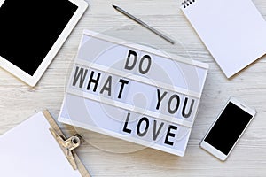 Workspace with clipboard, pencil, notepad, phone, tablet and modern board with text `Do what you love` on white wooden backgroun