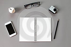 Workspace desk with blank notebook, pencil, eye glasses, small action camera, piggy bank and smart phone on gray background