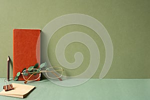 Workspace diary note, notepad, clip, pencil, eyeglasses, eucalyptus leaf on green desk. khaki wall background