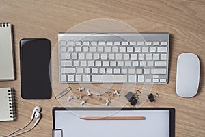 Workspace with diary or notebook and clipboard, mouse computer, keyboard, smart phone, Earphone, pencil, pen on wooden background