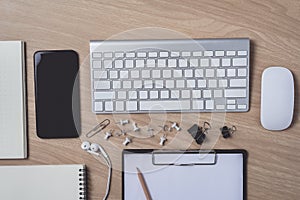 Workspace with diary or notebook and clipboard, mouse computer, keyboard, smart phone, Earphone, pencil, pen on wooden background