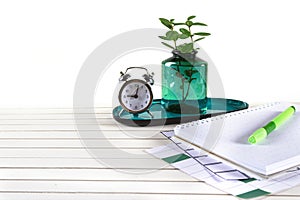 Workspace empty space with notebook, pen, alarm clock, plant potted and accessories on white wood desk background with office