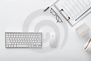 Workspace with keyboard mouse glasses papers. Flat lay White desk office workplace pc computer. White table silver