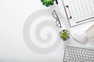 Workspace with keyboard mouse glasses papers green plants. Flat lay White desk home office workplace pc computer. White