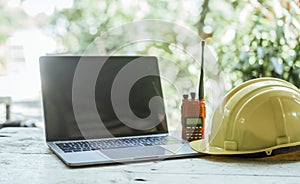 workspace with laptop, a hard hat on a wooden surface, likely belonging to a professional on a construction or engineering site