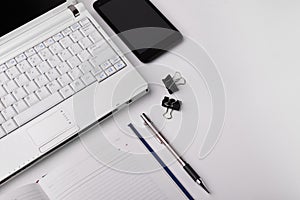 Workspace with laptop, smartphone, pen and datebook on white background. View from above