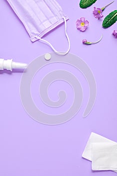 Workspace with napkins, pills, face mask, drops bottle and flowers on purple background.