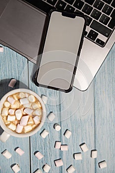 Workspace top view white cup of coffee and marshmallows White screen mobile phone laptop keyboard on wooden blue table