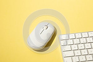 workspace with a white wireless mouse and computer keyboard on a yellow background