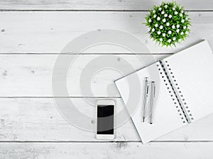 Workspace on white wood table top view copy space,Silver pen on blank page notebook and smartphone black screen