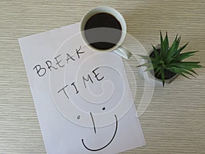 Worktable. Break Time Concept. Office desk table with break time note, coffee cup and flowers. Relaxation. Top view.