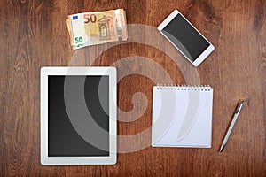 Worktop top view. white tablet and smartphone with a blank screen, money, notepad with pen and money