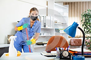 Workwoman of cleaning service in protective mask mopping floors in office