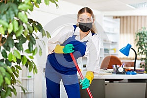 Workwoman of cleaning service in protective mask mopping floors in office