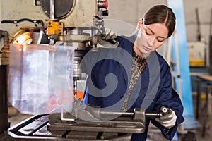 Workwoman drilling metal parts on bench drill