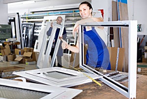 workwoman with plastic window frame in workshop giving thumbs up