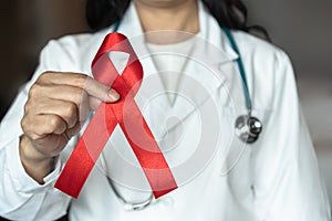 World aids day and national HIV AIDS and ageing awareness month with red ribbon on medical or surgical doctor\'s hand