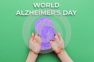 World Alzheimer& x27;s day. Female& x27;s hands holding a paper human head with puzzle ornament. Green background. Flat lay. The