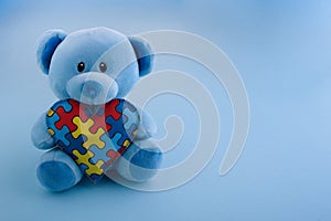 World Autism Awareness, concept with teddy bear holding puzzle or jigsaw pattern on heart on blue background