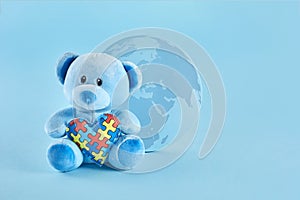 World Autism Awareness, concept with teddy bear holding puzzle or jigsaw pattern heart on blue background