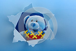 World Autism Awareness, concept with teddy bear holding puzzle or jigsaw pattern on heart in papaer cut hole