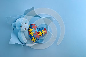 World Autism Awareness, concept with teddy bear holding puzzle or jigsaw pattern on heart in papaer cut hole