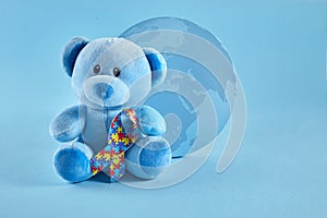 World Autism Awareness, concept with teddy bear holding puzzle or jigsaw pattern ribbon on blue background