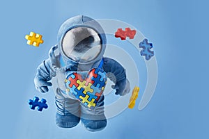 World Autism awareness day background. Blue plush astronaut toy with puzzle heart, autism symbol, on blue background
