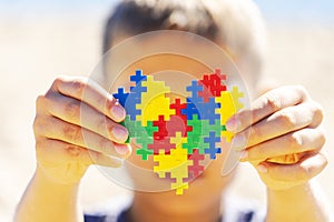 World autism awareness day concept. Boy holding colorful puzzle heart in front of his face