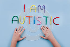 World Autism Awareness Day concept - multicolored letters, Am I Autistic - child hands playing against blue background