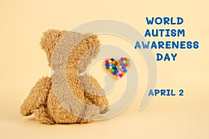 World Autism Awareness Day concept - sad teddy bear and multicolored defocused heart against yellow background. Autism spectrum