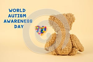 World Autism Awareness Day concept - sad teddy bear and multicolored defocused heart against yellow background. Autism spectrum