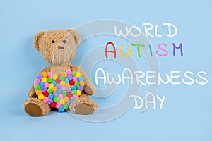 World Autism Awareness Day concept - sad teddy bear with multicolored heart sitting against blue background. Autism