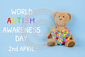 World Autism Awareness Day concept - sad teddy bear with multicolored heart sitting against blue background. Autism spectrum