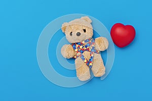 World Autism Awareness day, mental health care concept. Teddy bear with red heart and ribbon puzzle pattern. On blue background