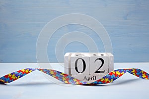 World Autism awareness and pride day with Puzzle pattern ribbon and calendar on blue wooden background