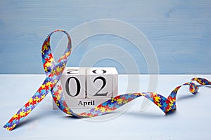 World Autism awareness and pride day with Puzzle pattern ribbon and calendar on blue wooden background