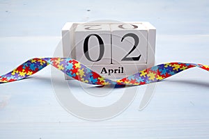 World Autism awareness and pride day with Puzzle pattern ribbon and calendar on blue wooden background