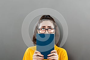 World Book Day. A portrait of a young thoughtful woman in glasses holding a book, looking up, covering half of her face