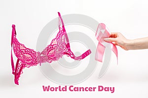 World cancer day. Pink lace bra on a white background and a woman's hand with a pink ribbon