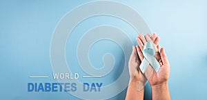 World diabetes day concept. Hand holding blue ribbon, symbolic bow color raising awareness in diabetes day on pastel background,